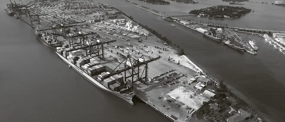 Aerial view of a container terminal: stacked containers, gantry cranes and a berthed container ship